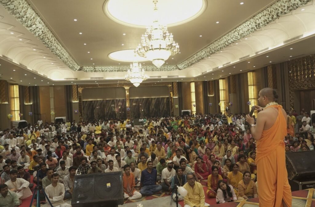 A packed hall of devotees listening to a scripture class